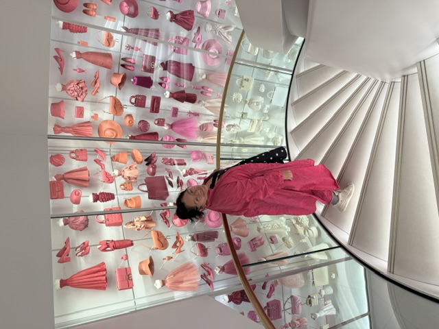 Liana on a spiral staircase in front of a pink fashion museum installation